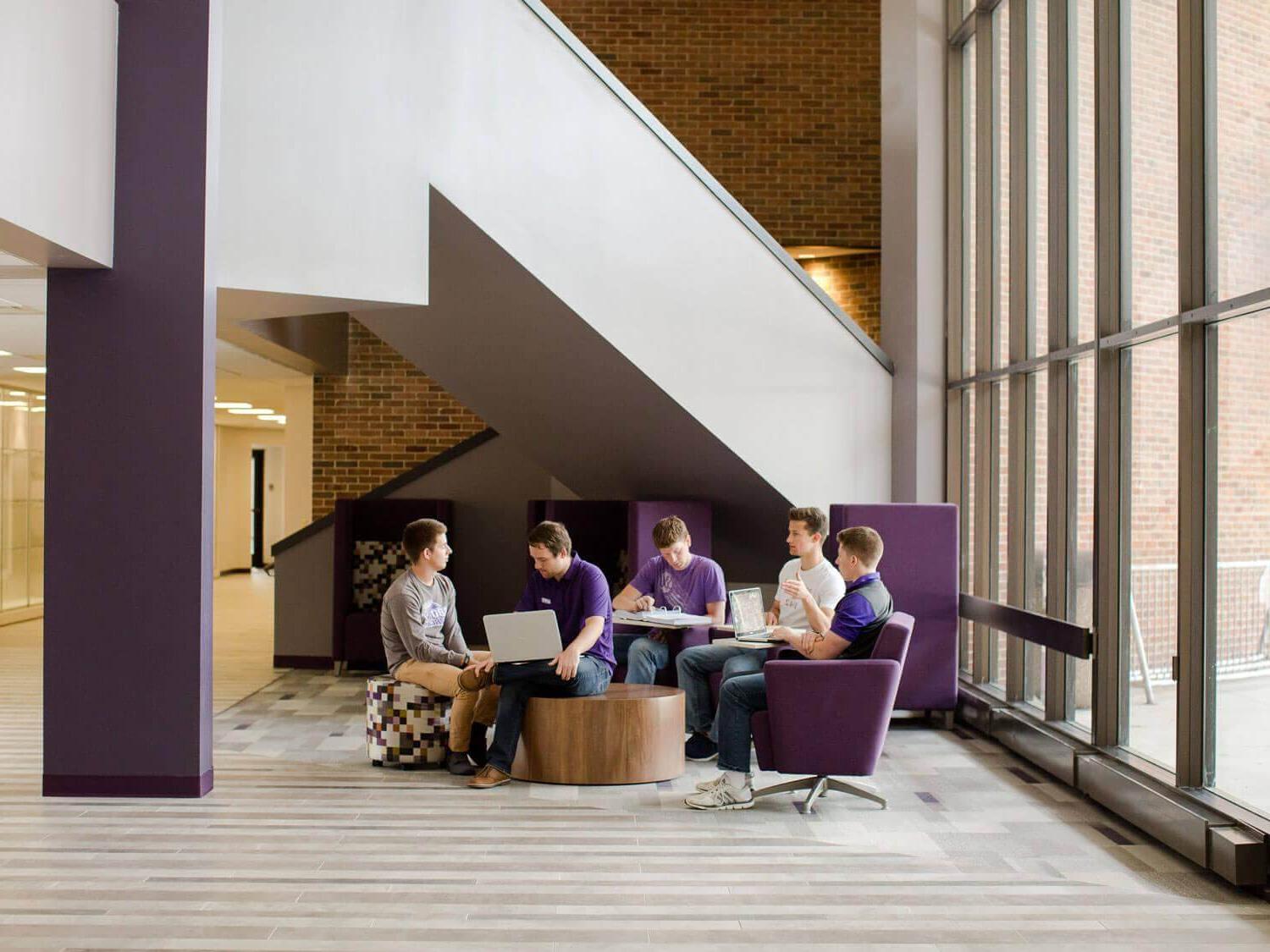 group of students gathered in chairs next to tall windows in building lobby